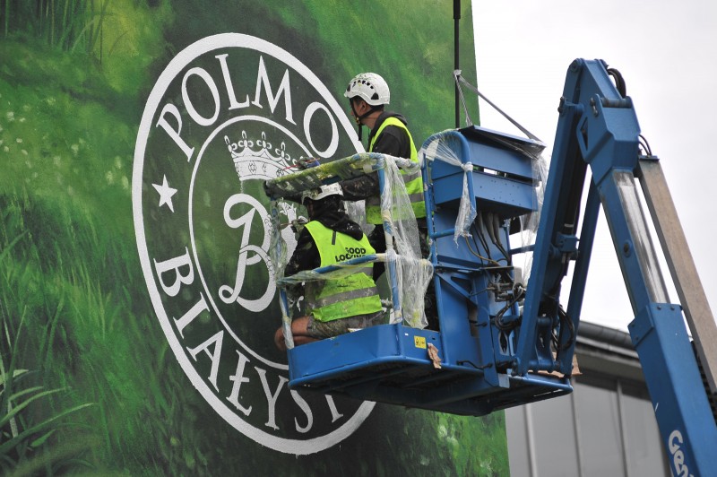 Logo Polmos Białystok malowane na podnośniku przez artystów na elewacji fabryki produkującej wódkę Żubrówkę | Mural wizerunkowy w Białymstoku na zlecenie Żubrówka | Portfolio